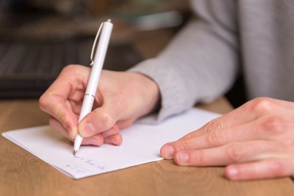 Person schreibt mit einem Stift auf ein Blatt Papier